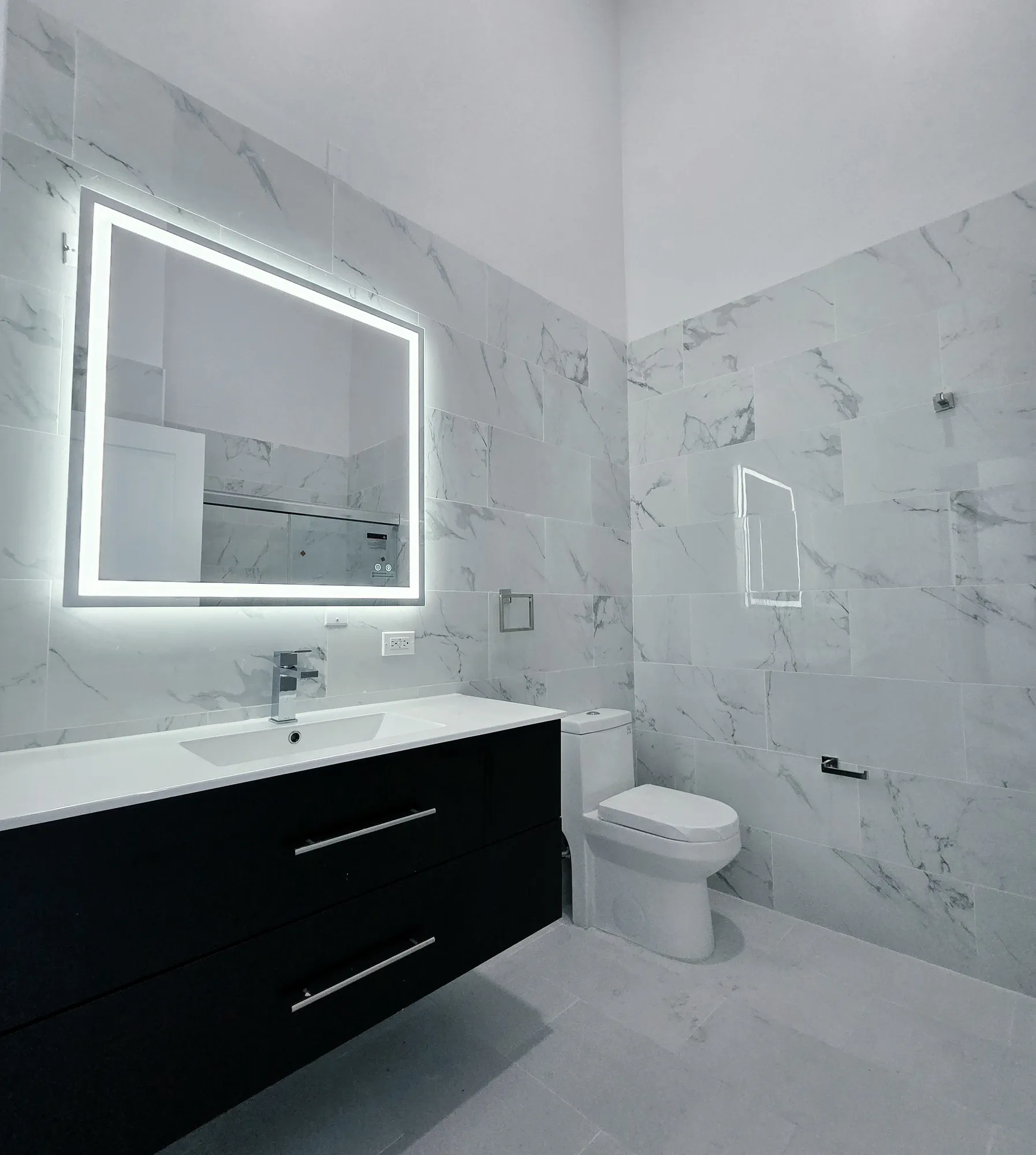 Bathroom with marble-style tile walls, floating black vanity, and backlit mirror