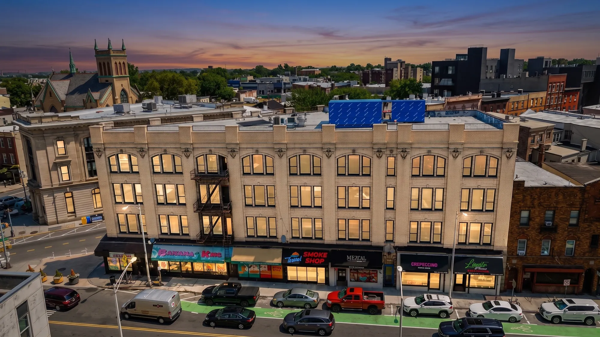 Full street elevation of 665 Newark Ave with storefronts and arched windows at dusk