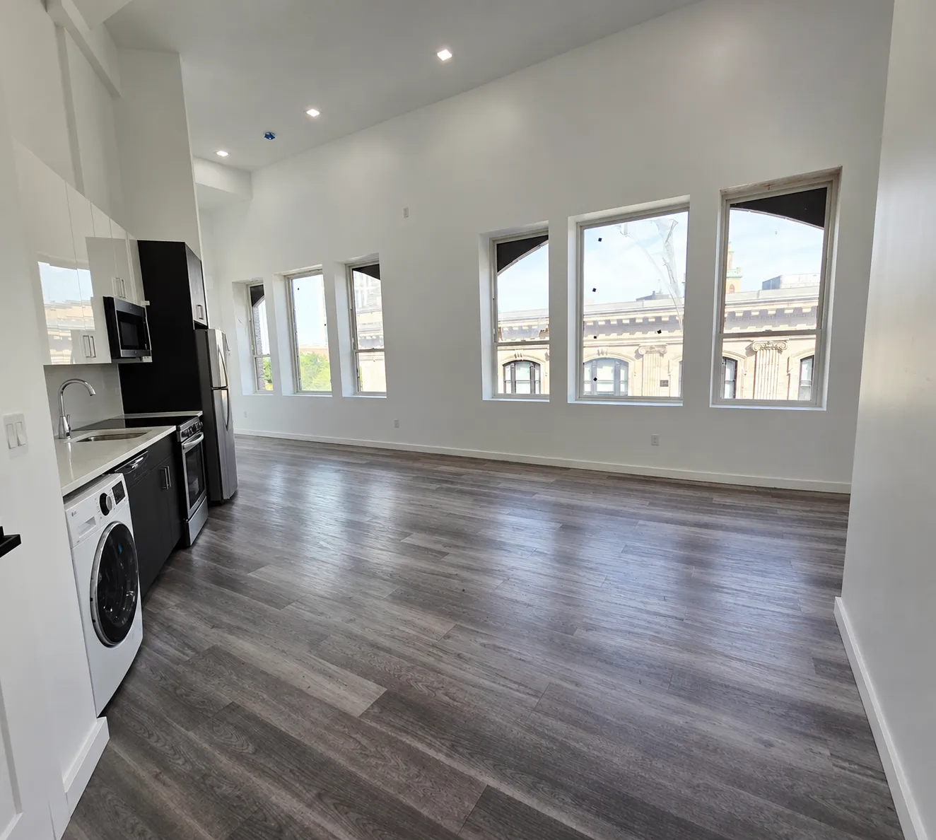 Open-plan living area with tall windows, recessed lighting, and new kitchen along the wall